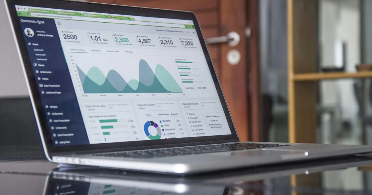 Open laptop on a glass table displaying an analytics dashboard with various charts and graphs.