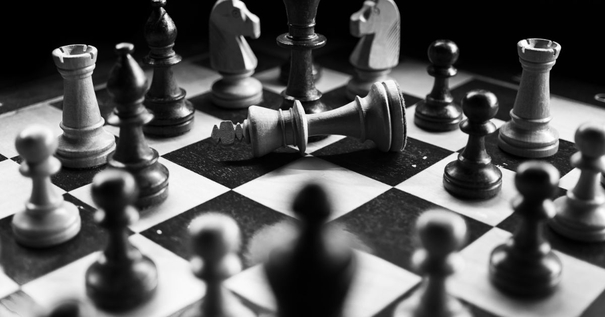 Chessboard with a fallen white king surrounded by various chess pieces.