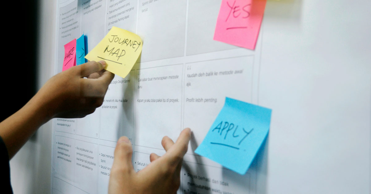 Hands placing sticky notes on a whiteboard with papers.
