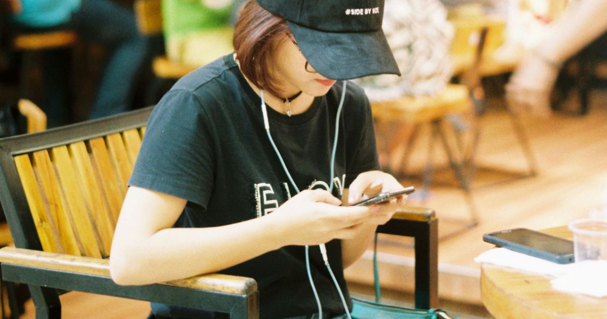 A woman with a hat and headphones sits at a table, focused and engaged in her activity.