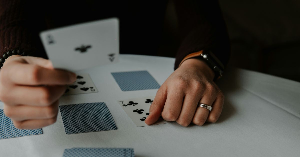 Hands playing a card game with an ace of spades and seven of clubs on display.