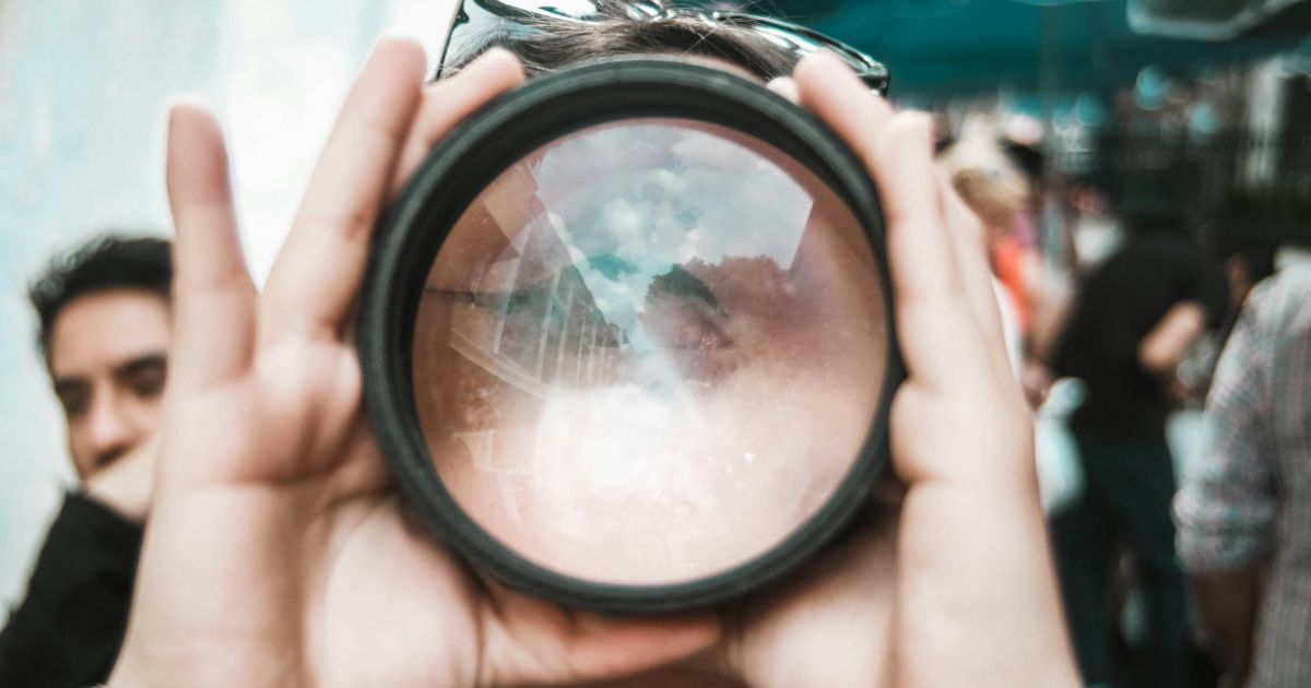 Person holding a reflective lens showing a sky and buildings.