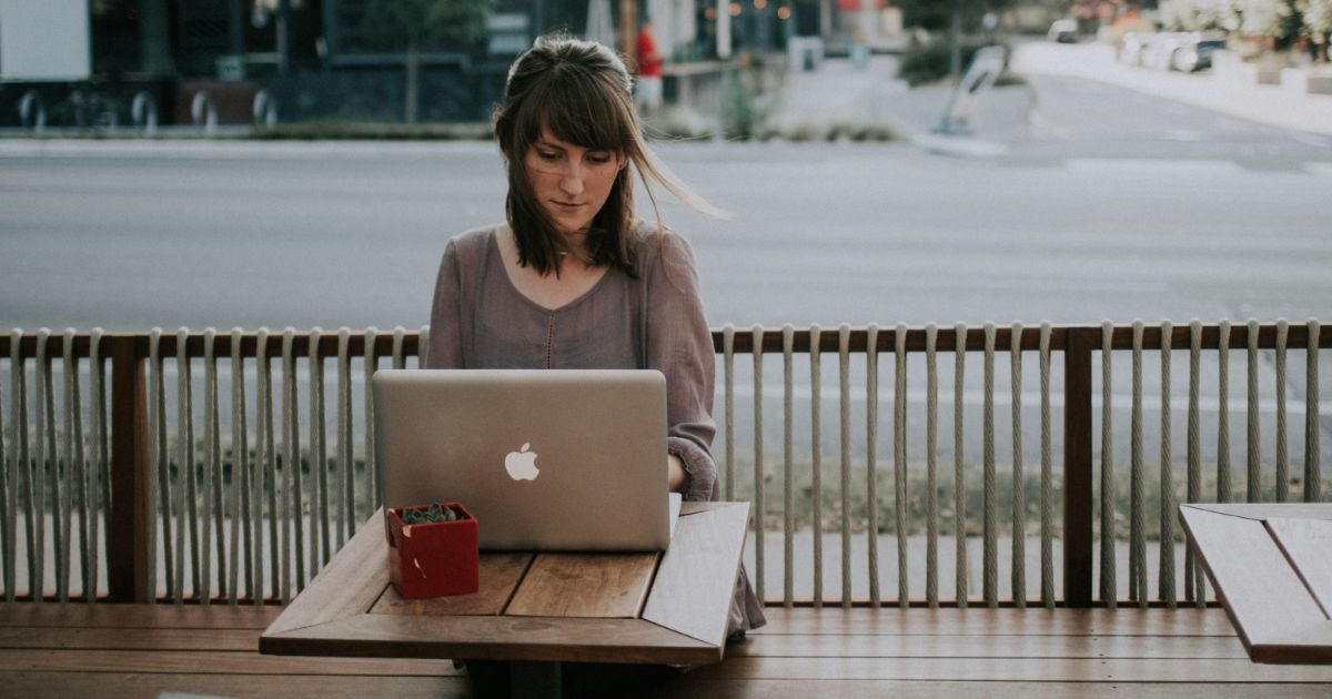 Person using a laptop at an outdoor table with a red planter box.