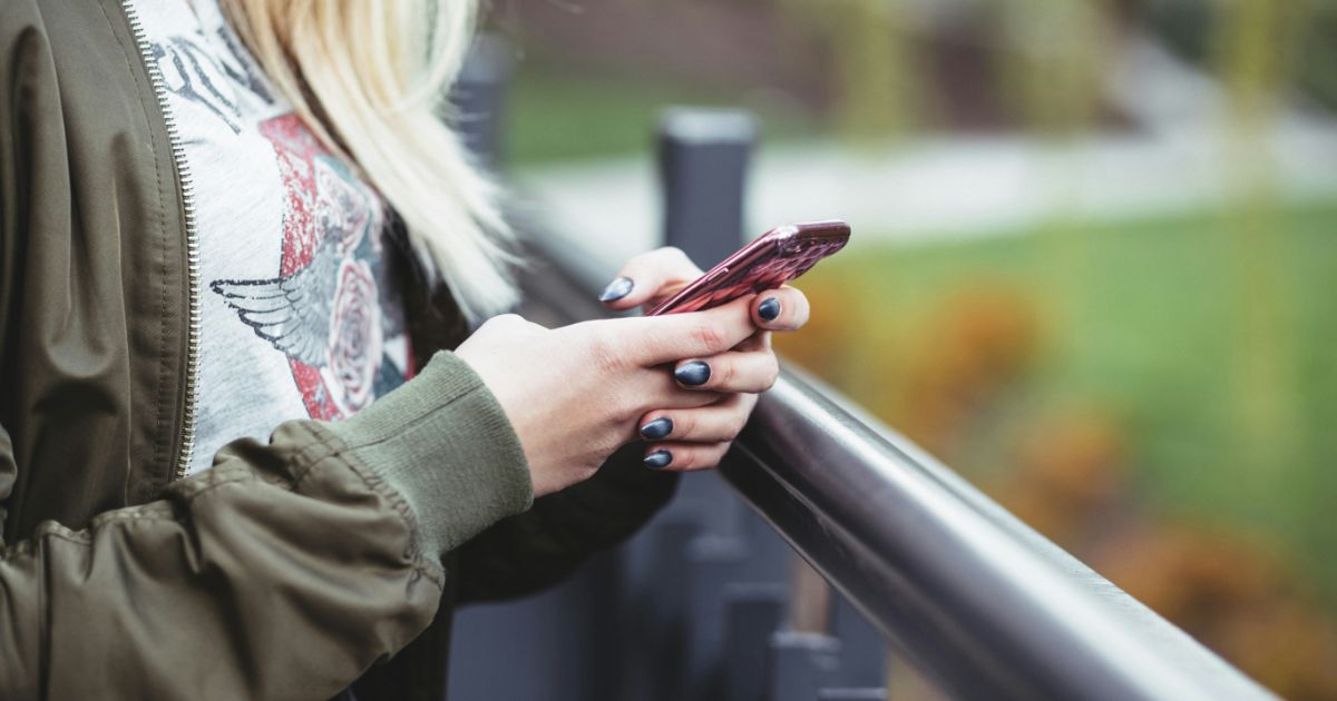Close-up of a person using a smartphone, wearing a green jacket and standing outdoors.