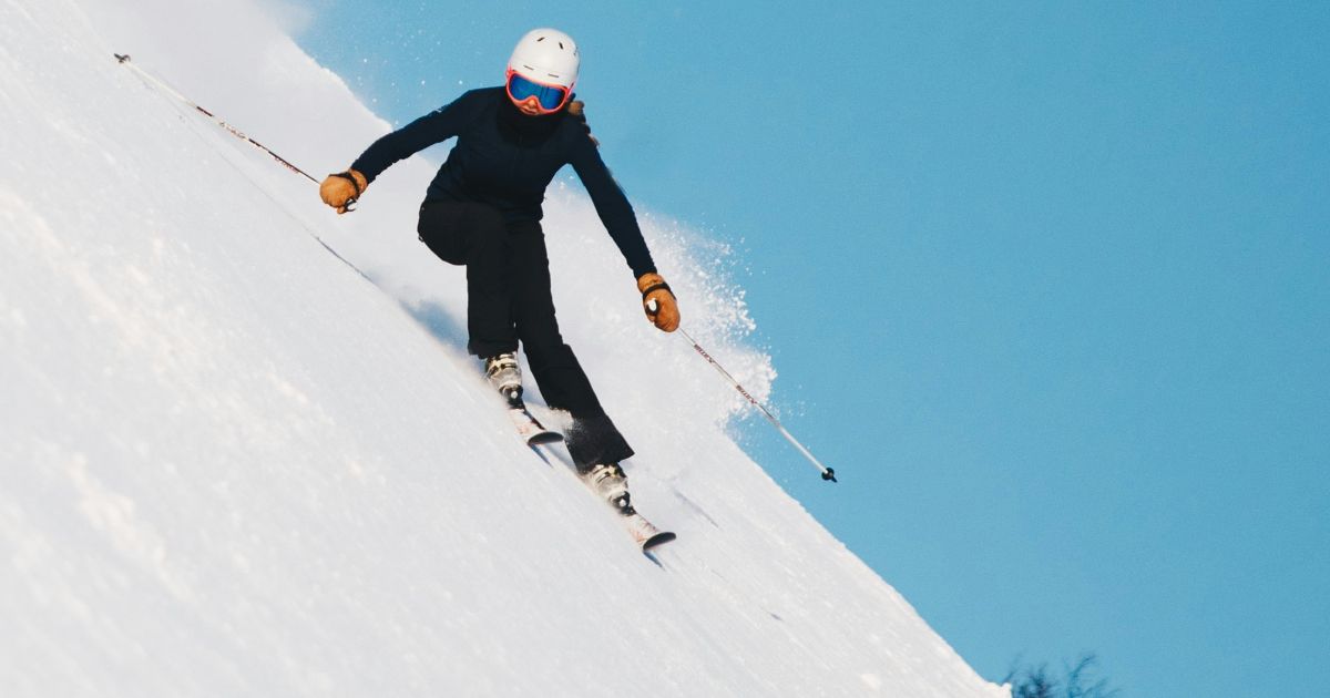 A skier gracefully descends a snowy slope, surrounded by pristine white snow and a clear blue sky.
