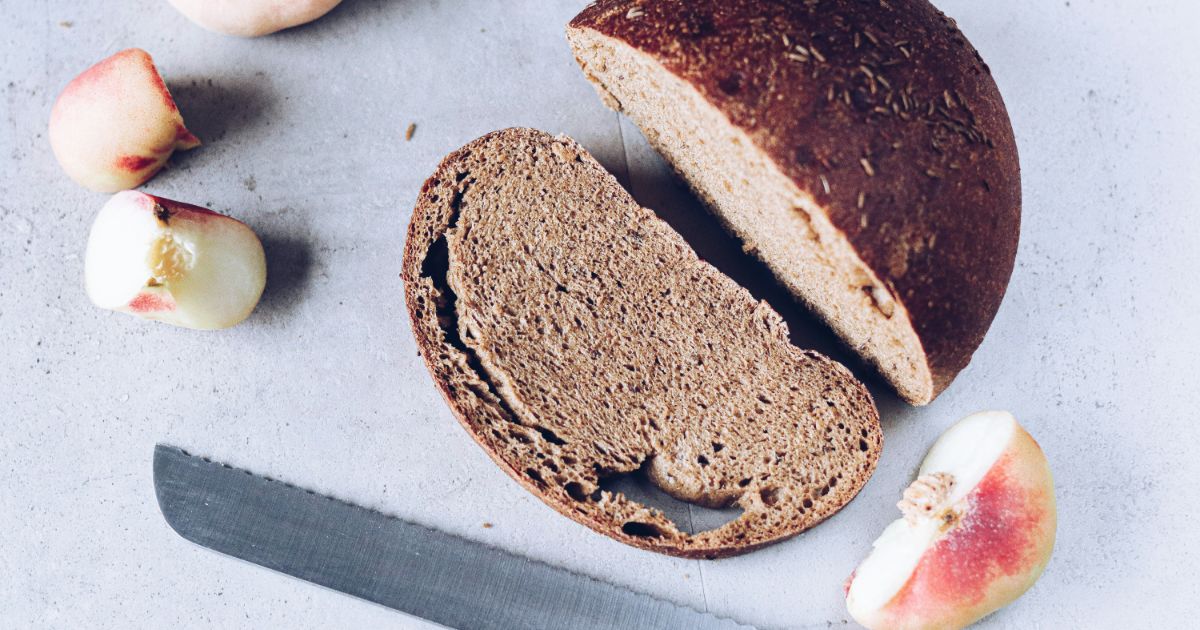 Sliced brown bread with peaches and a serrated knife on a light surface.