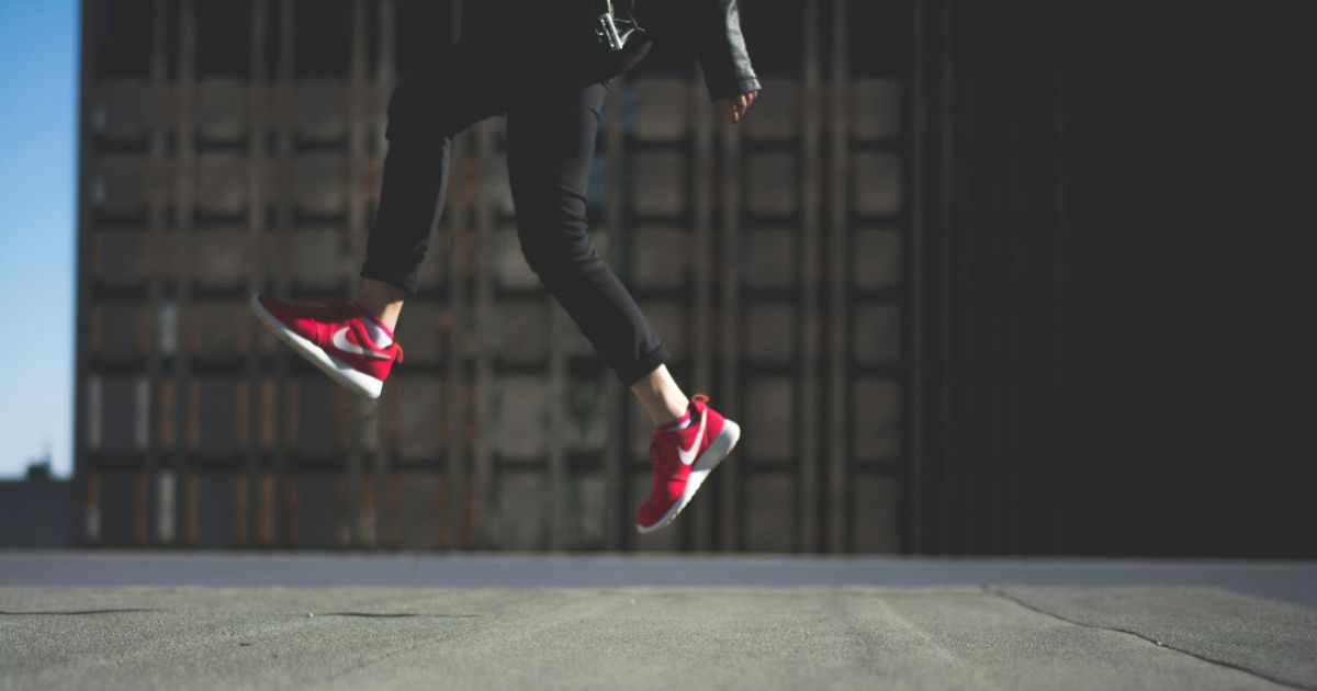 Person in mid-jump wearing red athletic shoes against a cityscape background.
