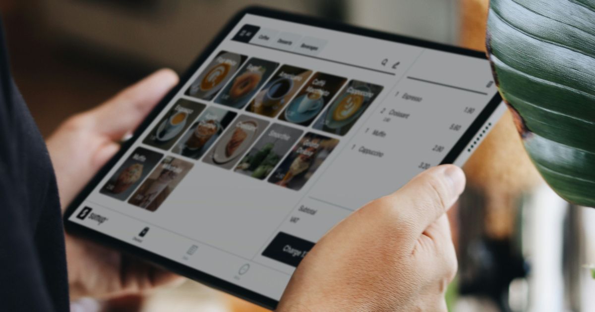 Person holding a tablet displaying a digital menu with food and drink categories and prices.