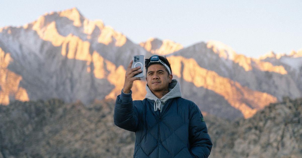 A man captures a selfie with a stunning mountain backdrop, showcasing his phone addiction and enjoyment of the experience.