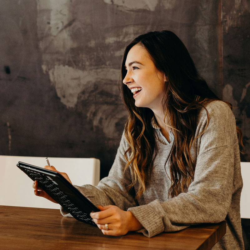 brooke-cagle-JBwcenOuRCg-unsplash A woman sitting at a table, focused on her tablet, with a cozy atmosphere around her.