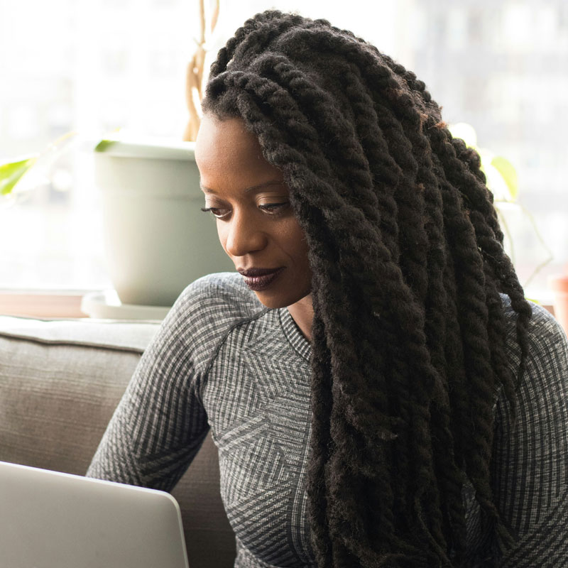 christina-wocintechchat-com-fjza4oBV8ic-unsplash A woman with dreadlocks sits comfortably on a couch, focused on her laptop, creating a cozy and productive atmosphere.