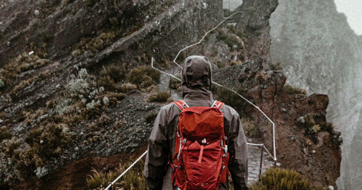 Person with a red backpack on a misty mountain trail.