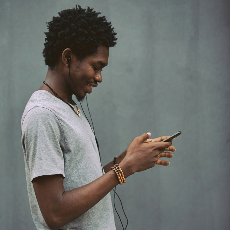 emmanuel-ikwuegbu-81fRHbVliQI-unsplash A young man enjoys music on his phone, lost in the rhythm with a smile on his face.