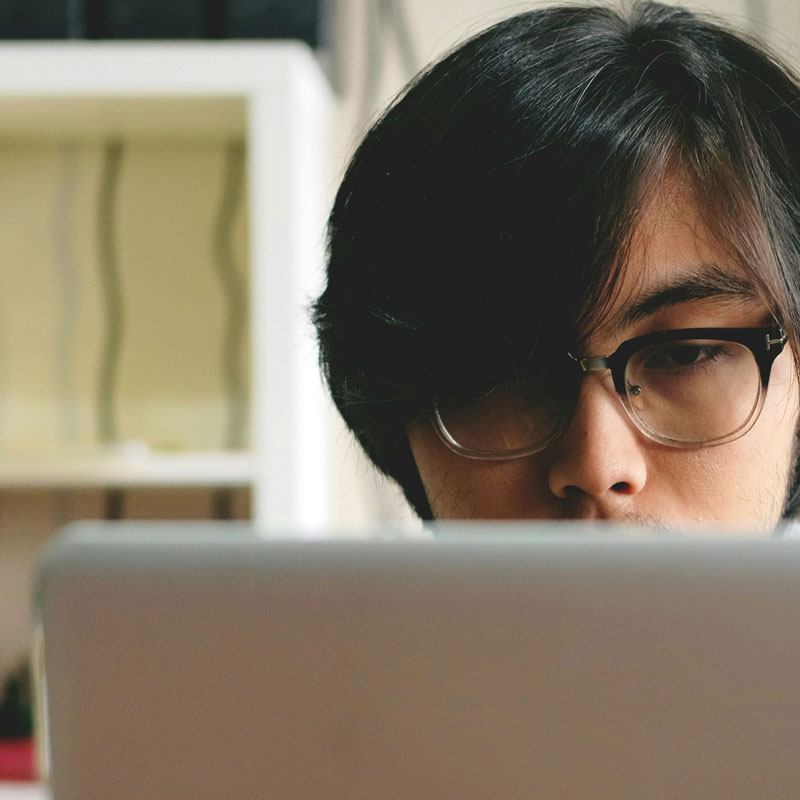 firza-pratama-b5fm9Lvf3F4-unsplash A man wearing glasses is absorbed in his laptop, showcasing concentration and engagement with his digital task.