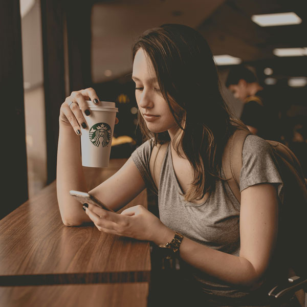 guilherme-stecanella-4jy1DQKmX2w-unsplash A woman sitting at a cafe, focused on her phone, enjoying her time in a cozy atmosphere.