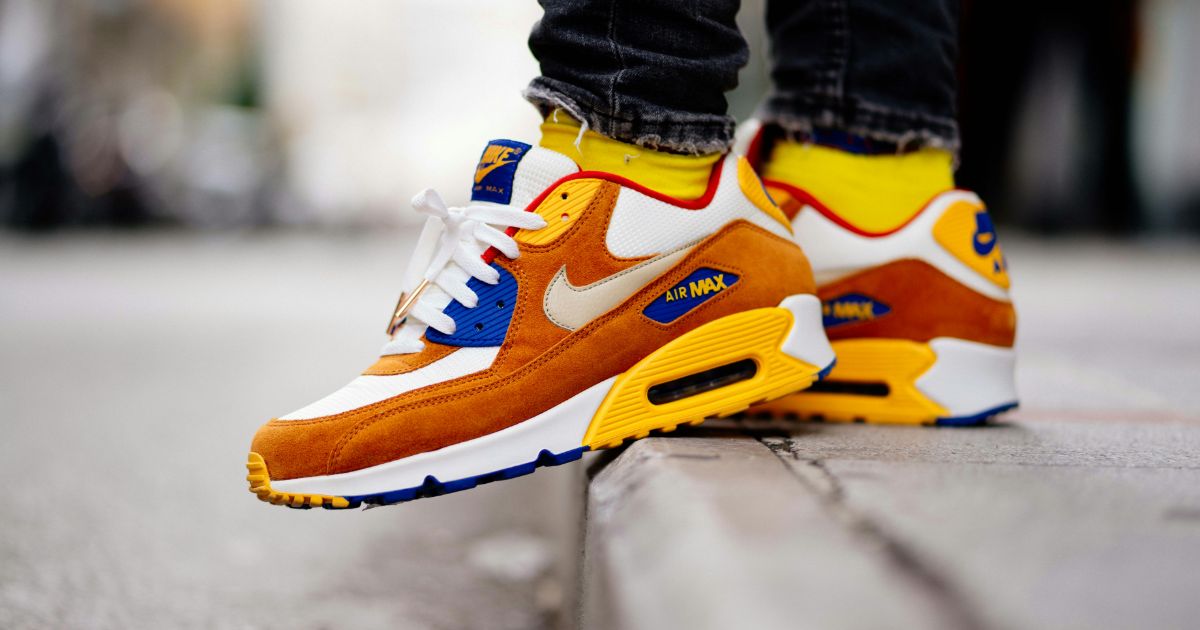 Orange and white sneakers with blue and yellow accents on a street curb.