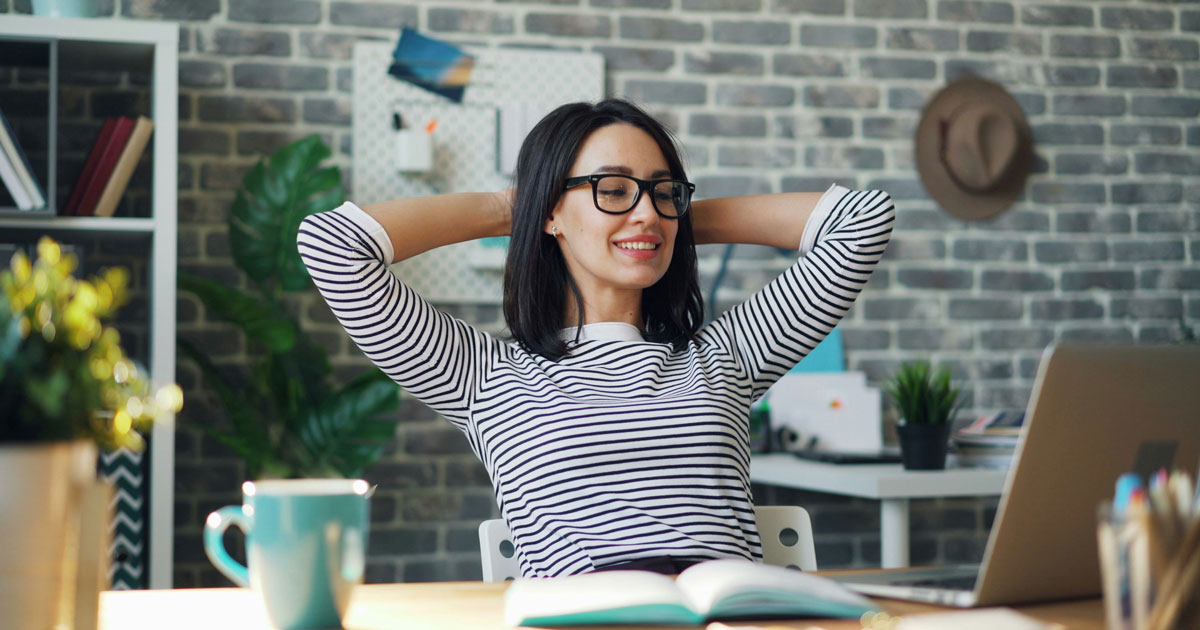 A woman in glasses sits at a desk, arms raised, embodying the concept of cognitive fluency in UX design.