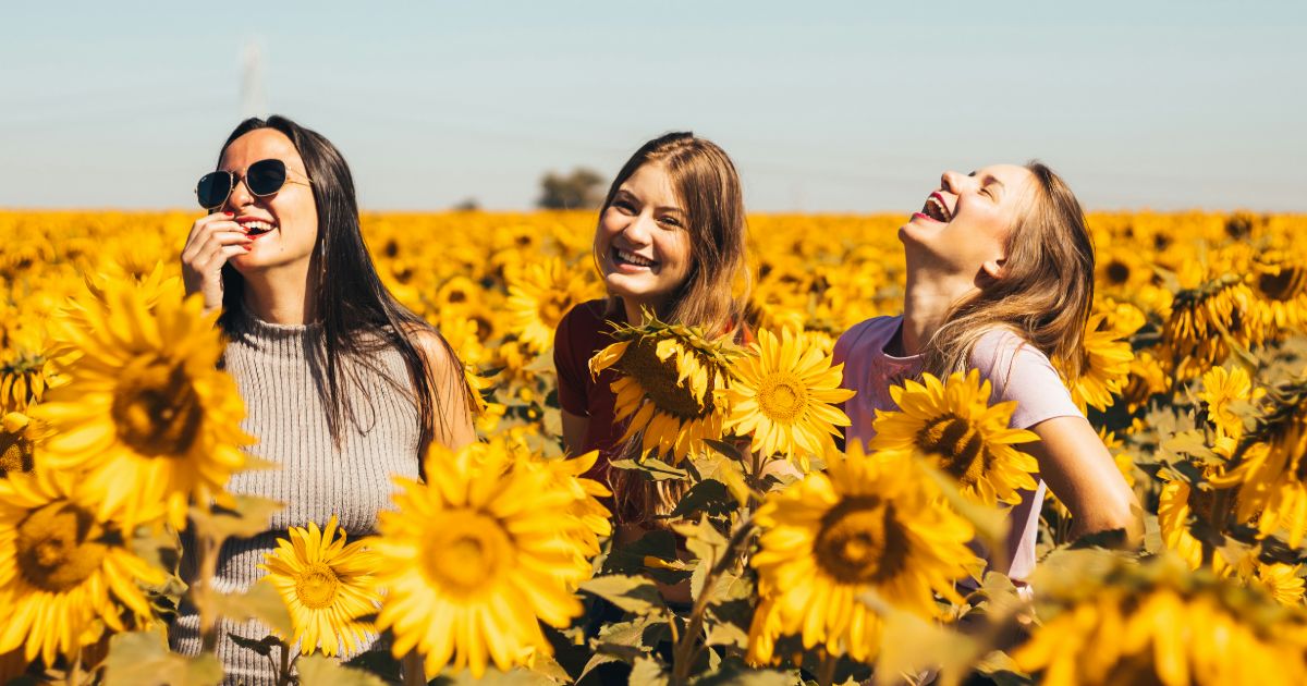 Three women joyfully laughing together in a vibrant sunflower field, showcasing Social proof in UI design.