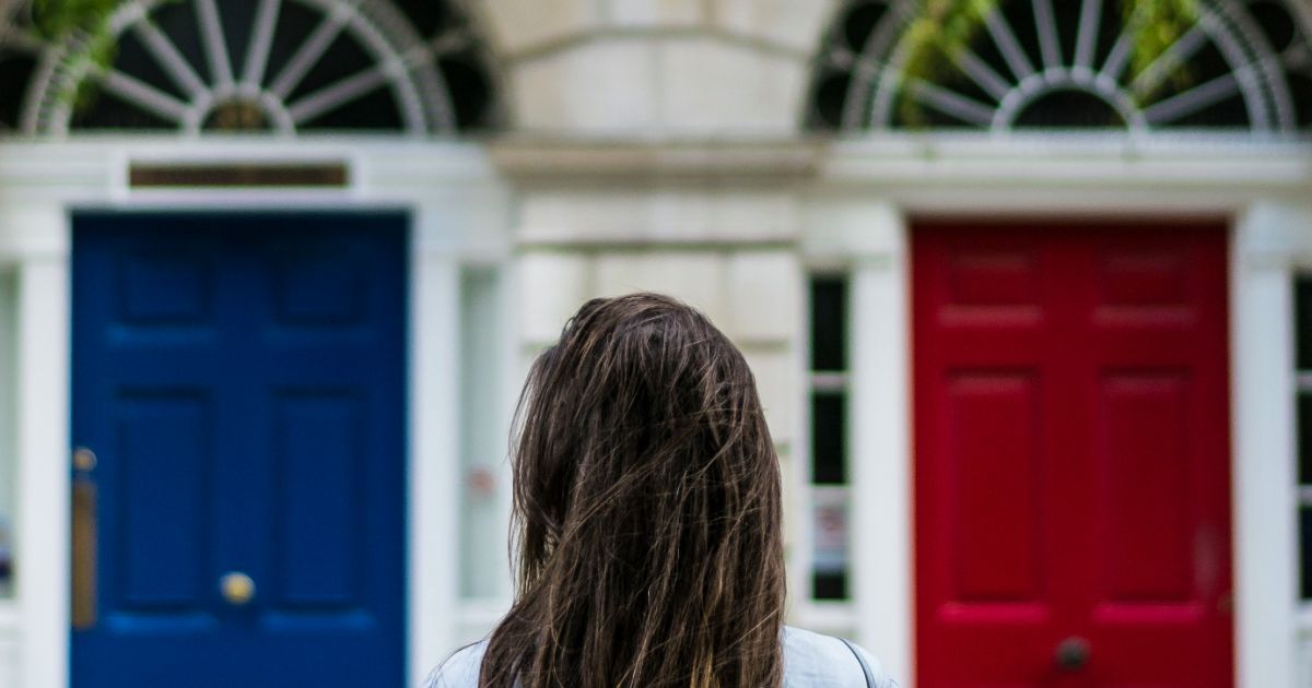 A woman with long hair stands before two bold doors, one red and one blue, showcasing the Paradox of Choice in UX