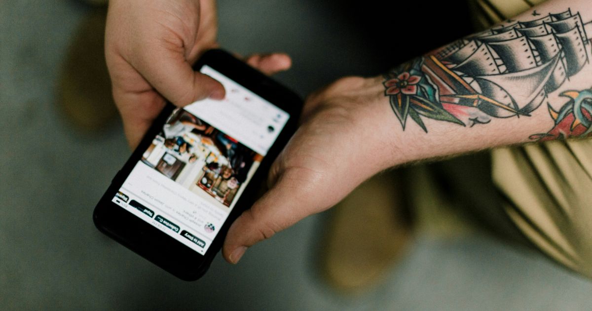 A tattooed person holding a smartphone, looking engaged while interacting with the device representing IA in Infinite Scroll.