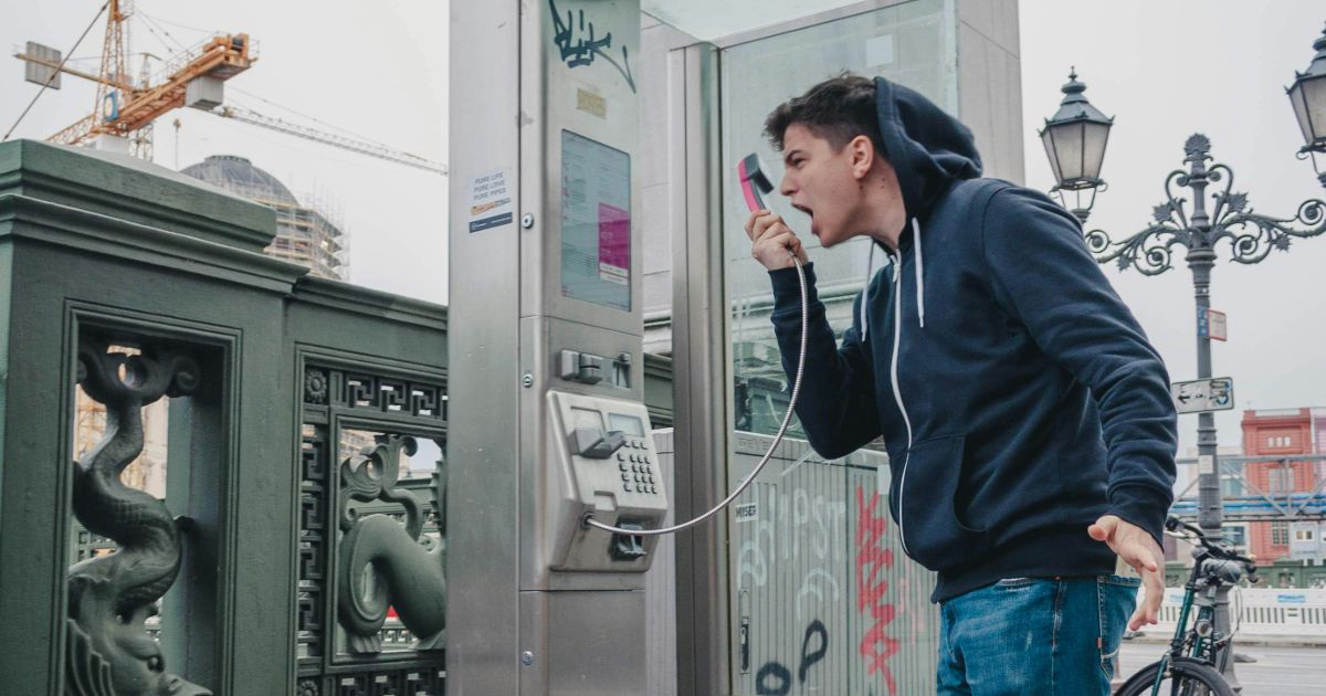 A man talks on his phone, positioned in front of a pay phone, illustrating UX leadership for quiet designers.