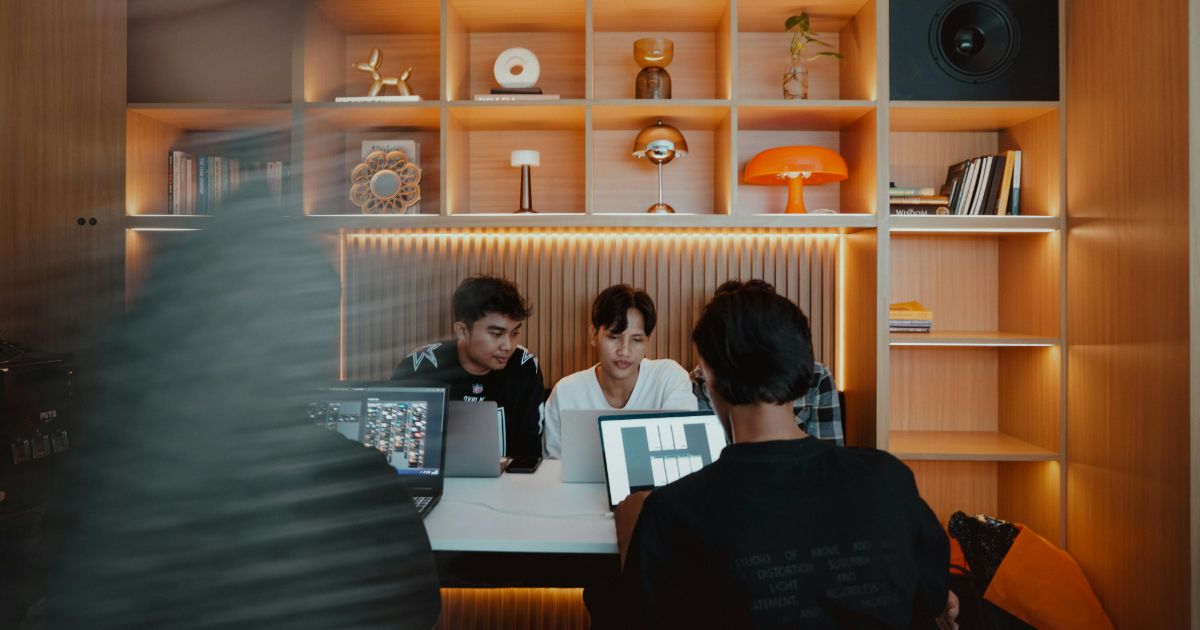 Three people collaborate at a table, focused on a computer screen in a bright, modern workspace demonstrating soft skills in UX leadership.