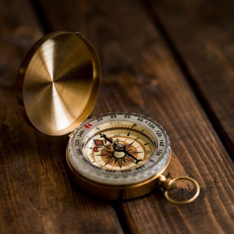 An antique gold compass resting on a rustic wooden table, showcasing its intricate design and vintage charm.