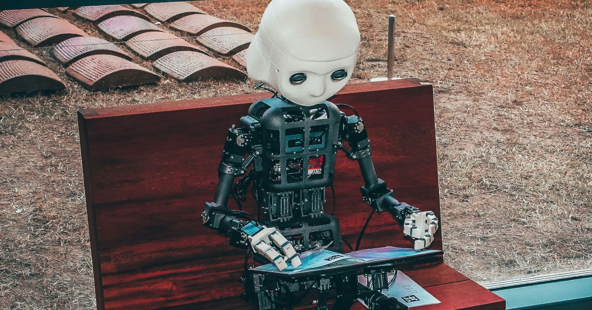 A robot sits on a bench, focused on a laptop, blending technology with a serene outdoor setting representing AI-assisted UX research synthesis.
