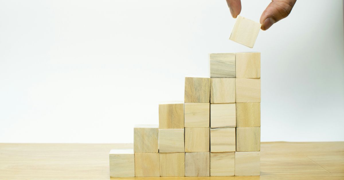 A person stacking wooden blocks on a wooden staircase, focusing on balance and structure just like goal-gradient effect in UX.