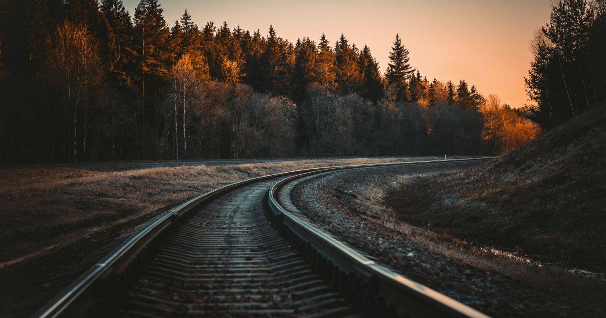 A train track stretches through a forest, illuminated by the warm hues of a sunset in the background representing contextual information architecture.