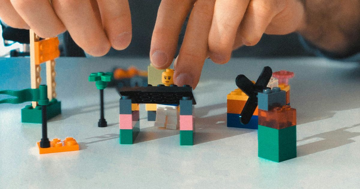 A man joyfully builds a colorful structure with various LEGO bricks on a table