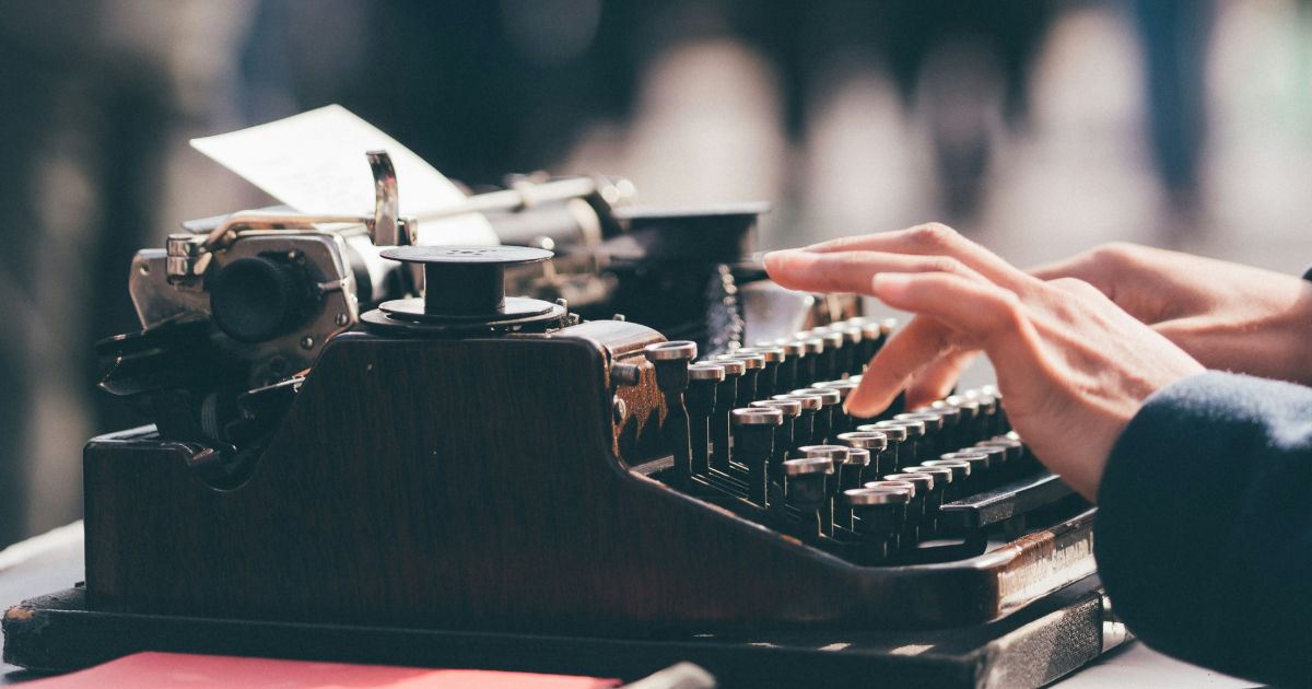 person focused on typing on a vintage typewriter, with fingers poised over the keys, capturing a moment of creativity representing accessible UX writing.
