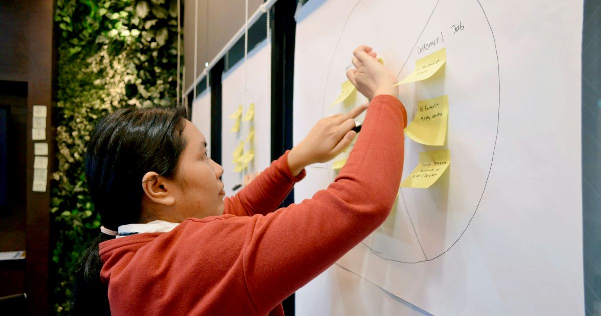 A woman actively writes on a whiteboard, illustrating her ideas with enthusiasm representing UX Research Debt.