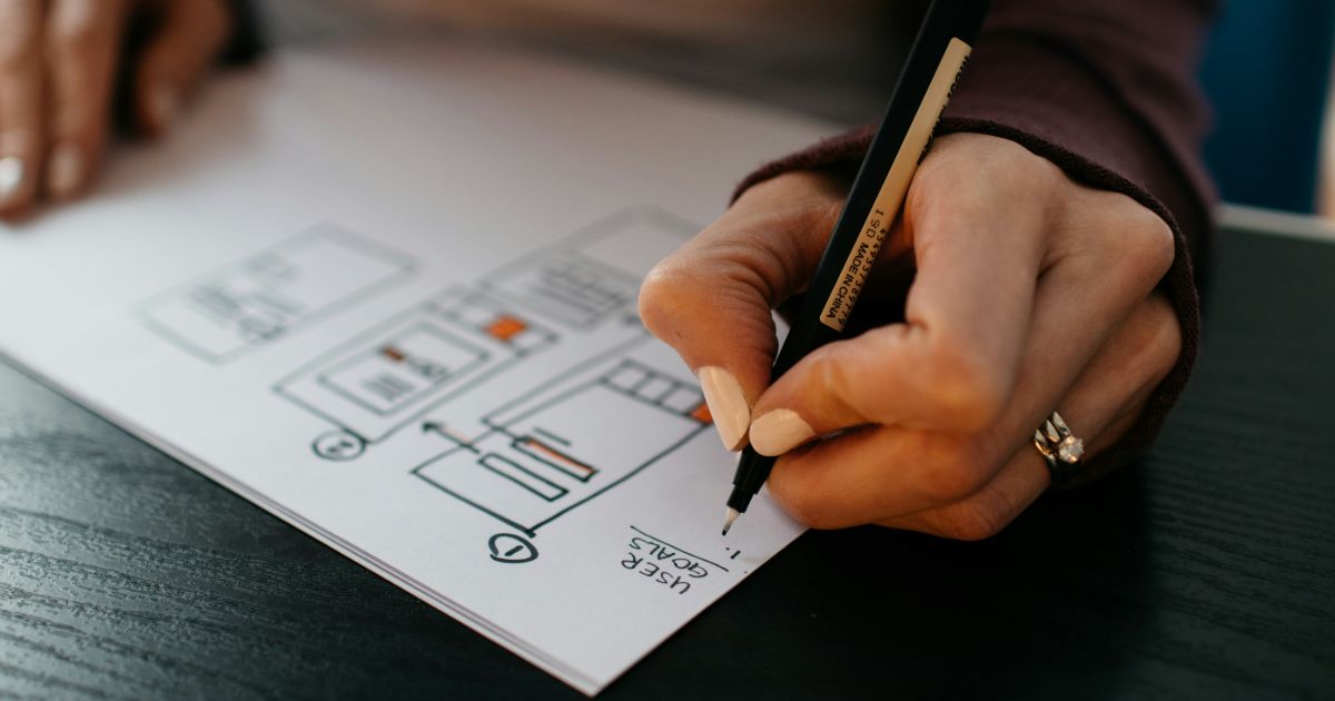 A person is focused on drawing on a sheet of paper with a pen, showcasing their artistic skills representing no-code UX.