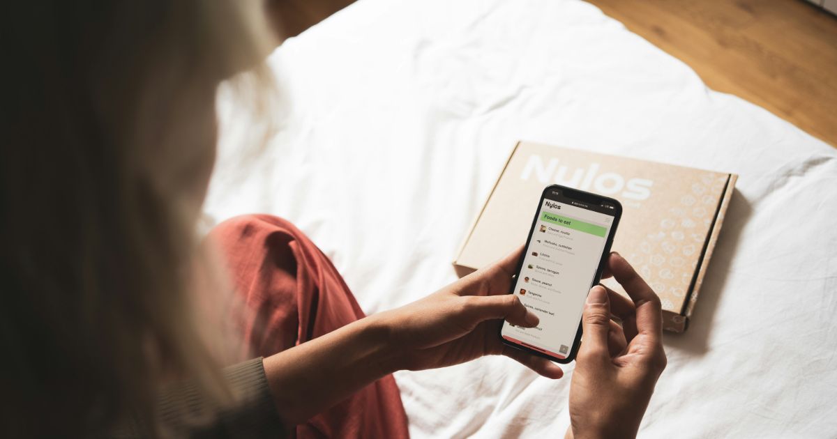 A woman sitting on a bed, using her phone to check her email, surrounded by soft bedding and a cozy atmosphere representing cognitive bias in personalization.