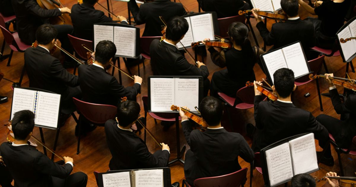 An orchestra of musicians performing together, showcasing various instruments and a conductor leading the ensemble representing inclusive visual hierarchy.