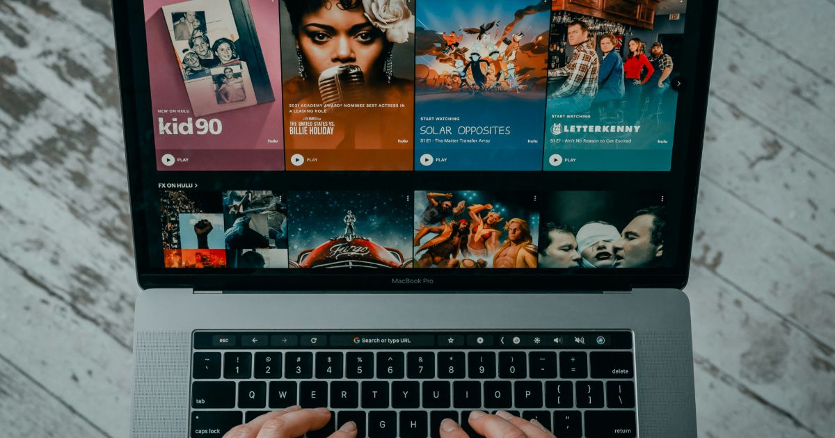 A person types on a laptop in front of a large movie screen, focused on their work amidst a cinematic backdrop representing Sunk cost fallacy.